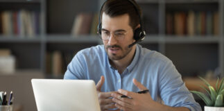 Confident man teacher coach wearing headset speaking, holding online lesson, focused student wearing glasses looking at laptop screen, studying, watching webinar training, listening to lecture
